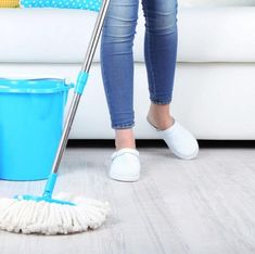 a woman is using a mop to clean the floor in front of a couch