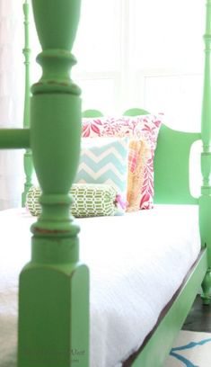 a bed with green headboard and foot board next to window in bright bedroom area