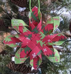 a green and red ornament hanging from a tree with pine cones in the background