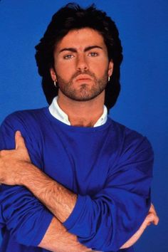 a man with his arms crossed posing for a photo in front of a blue background