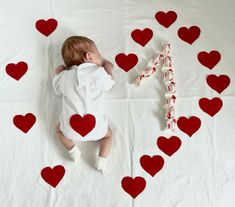 a baby laying on top of a white sheet covered in red hearts