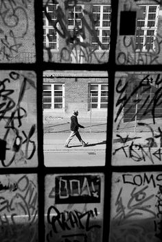 black and white photograph of person walking past window with graffiti on it