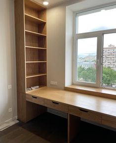 an empty desk in front of a large window with city view behind it and wooden shelves