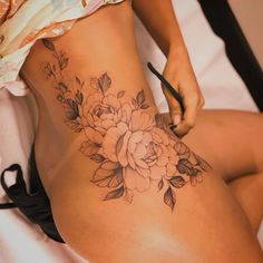 a woman with a flower tattoo on her stomach is sitting down and writing in a pen