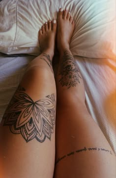 a woman's legs with tattoos on them laying on a bed next to a pillow