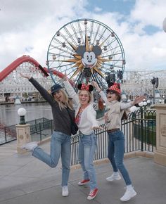 three girls are posing in front of a ferris wheel with mickey mouse ears on their heads