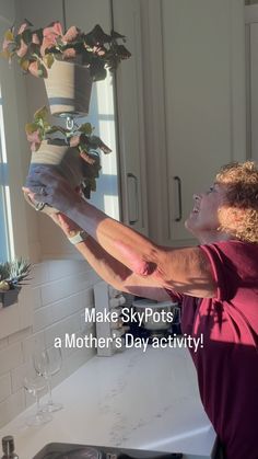 a woman is holding up a vase with flowers on it in the middle of a kitchen