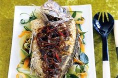 a white plate topped with fish covered in sauce and veggies next to silverware