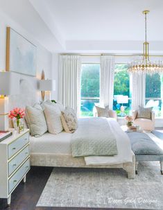 a bedroom with a large bed, chandelier and two chairs in front of the window