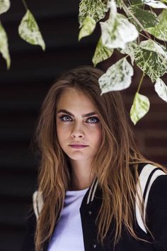 a woman with long brown hair and blue eyes is standing under a leafy tree