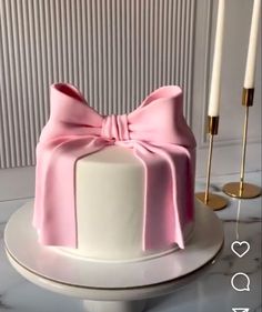 a white cake with a pink bow on top and two candles in the back ground