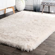 a white area rug in the corner of a room next to a chair and vase