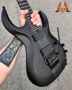 a person holding a black electric guitar in their left hand and tattoo on his right arm