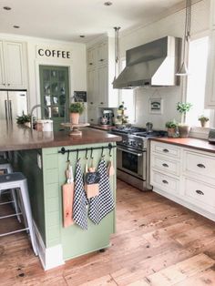 a kitchen with white cabinets and green island in the center, hanging tea towels on hooks