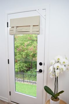 a white door with a window covering over it and flowers in front of the door