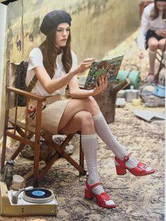 a woman sitting in a chair reading a book with her feet up on the ground