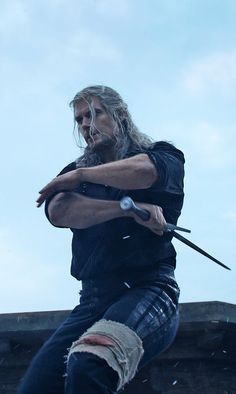 a man with long hair and beard holding an arrow in his hand while standing on top of a roof