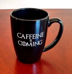 a black coffee mug with the words caffeine is coming on it sitting on a wooden table