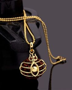 a gold necklace with a bell hanging from it's side on a black surface