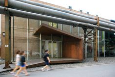 two people walking past a building with large windows on the front and side of it