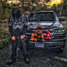 a person standing next to a truck with stuffed animals on the hood and in front of it