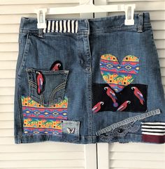 a pair of blue jean shorts with colorful birds and hearts on them hanging from a white door