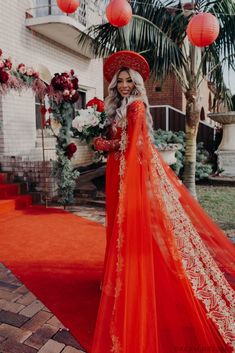 a woman in an orange dress and red hat standing on a red carpet with flowers