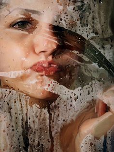 a woman's face is shown through the rain drops on her glass window as she brushes her teeth