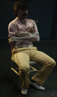 a man sitting on top of a chair with a rope wrapped around his neck and legs