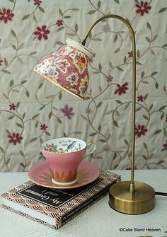 a pink cup and saucer sitting on top of a table next to a lamp