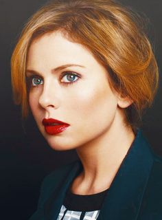 a woman with red lipstick and a suit jacket on posing for a photo in front of a black background