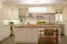 a large kitchen with white cabinets and wooden counter tops, along with two stools in front of the island