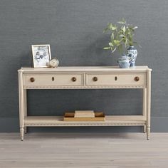 a white table with two drawers and a potted plant on it next to a gray wall