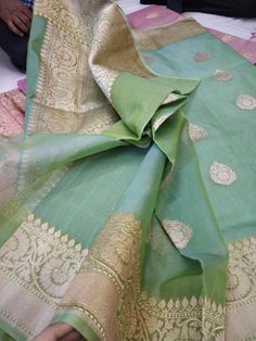 a green and gold sari is laying on top of a bed with two people sitting in the background