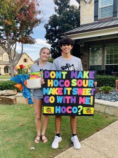 two people standing in front of a house holding a sign