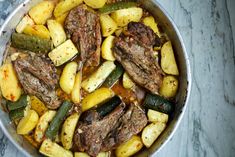 a pan filled with meat, potatoes and zucchini