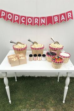 a table topped with lots of cupcakes next to a sign that says popcorn bar