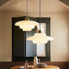 three lights hanging from the ceiling above a table with plates and cups in front of it