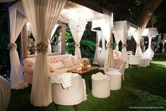 an outdoor wedding venue with white drapes and couches, chandeliers and tables