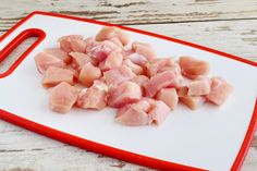 raw chicken pieces on a cutting board ready to be cut into bite sized pieces with a red handle