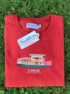 a red t - shirt with the name and image of a building on it is laying in the grass