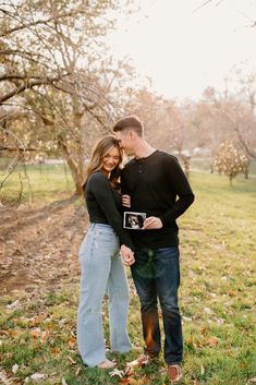 a man and woman standing in the grass with their arms around each other while holding an old photo