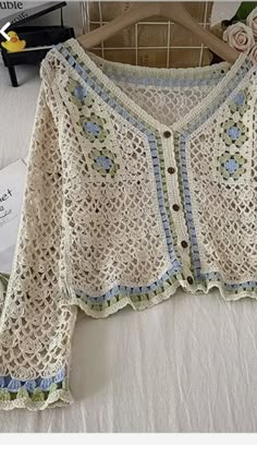 a white crocheted sweater sitting on top of a bed next to a cardigan