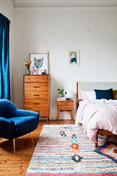 a bed room with a neatly made bed next to a blue chair and a dresser