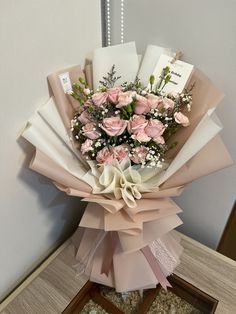 a bouquet of pink roses and baby's breath wrapped in white paper on top of a table