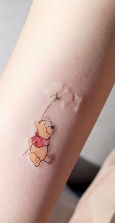 a small winnie the pooh tattoo on someone's left arm with a dandelion