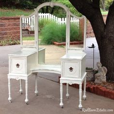 a white vanity table with a mirror on it next to a tree and brick wall