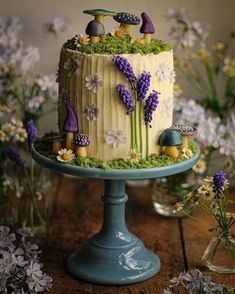 a cake decorated with lavenders and mushrooms on a blue pedestal next to flowers in vases