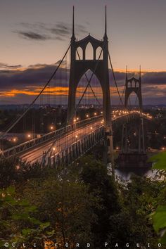 the sun is setting over the bridge and it's lights are on