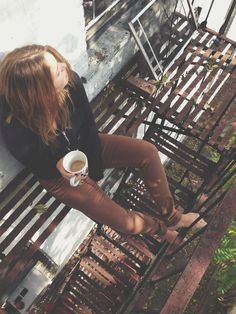 a woman sitting on a wooden bench holding a cup of coffee